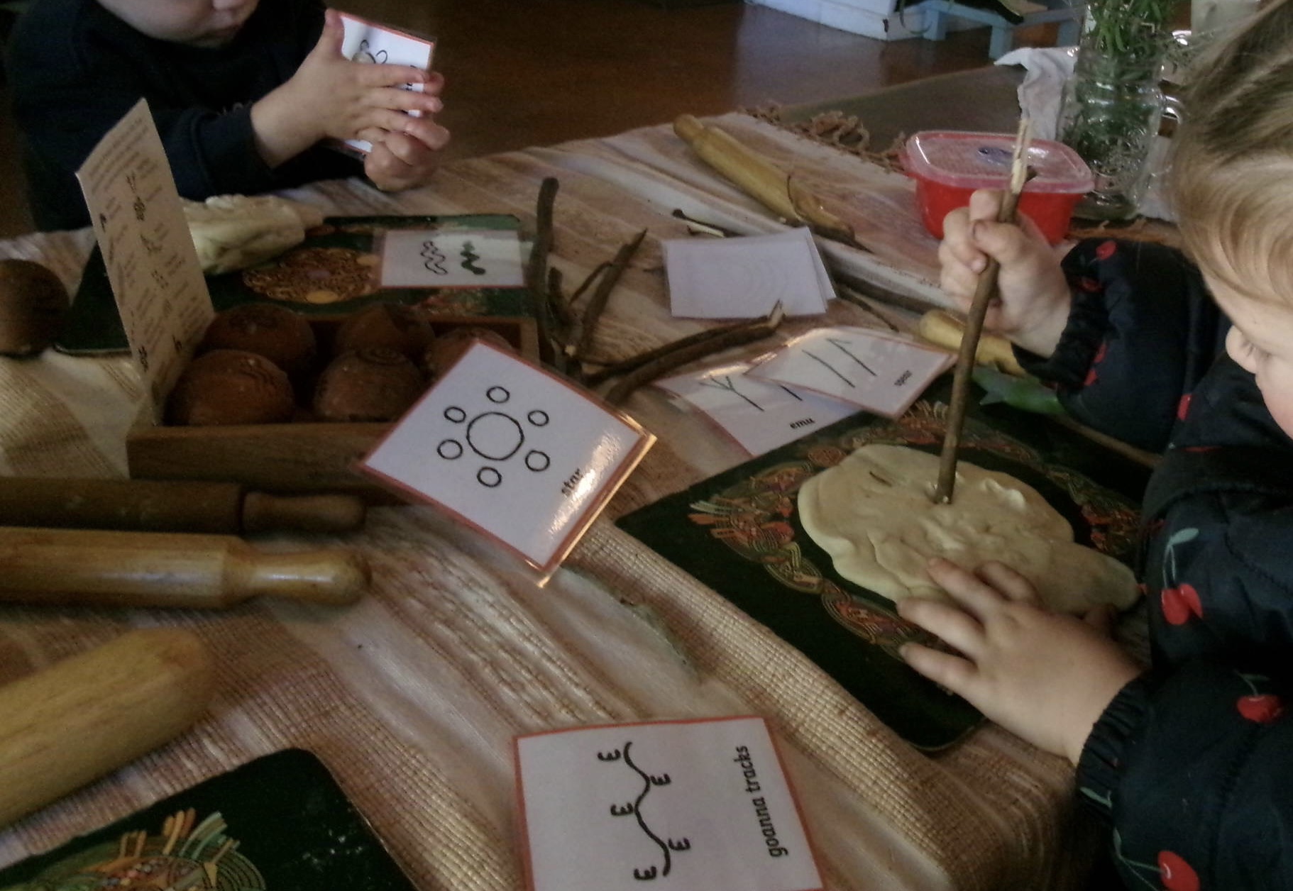 Children making First Nations symbol imprints in clay with goanna tracks reference cards