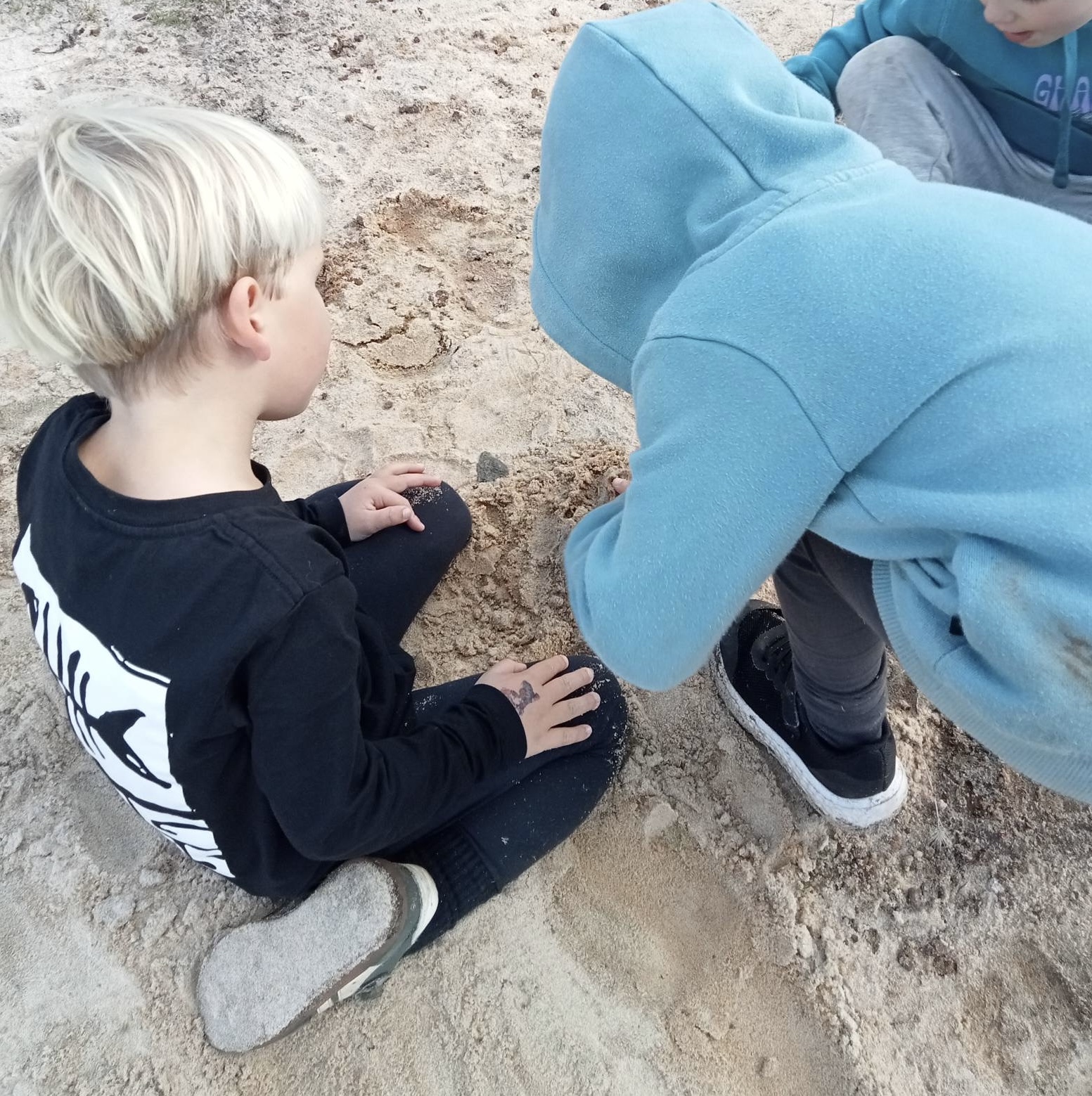 Two children closely investigating the sandy ground together