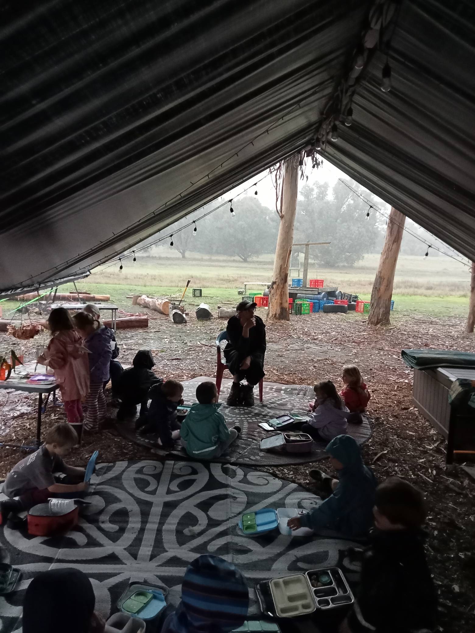Morning meeting with educator and children under the outdoor tent structure